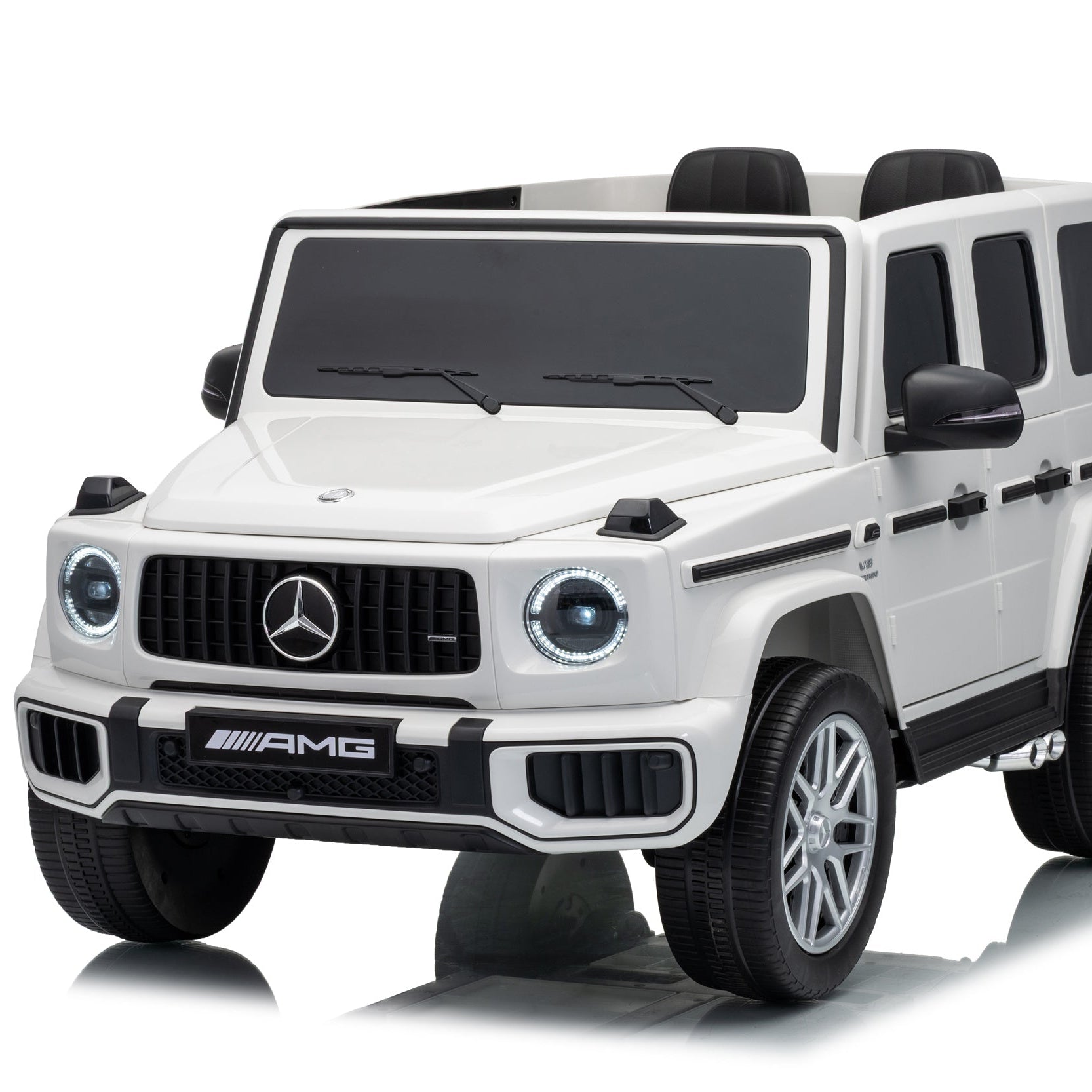 A white Mercedes-Benz AMG children's ride-on toy car styled like a G-Class SUV, featuring a black front grille, black wheels, and black side trim, shown on a white background with a reflection.