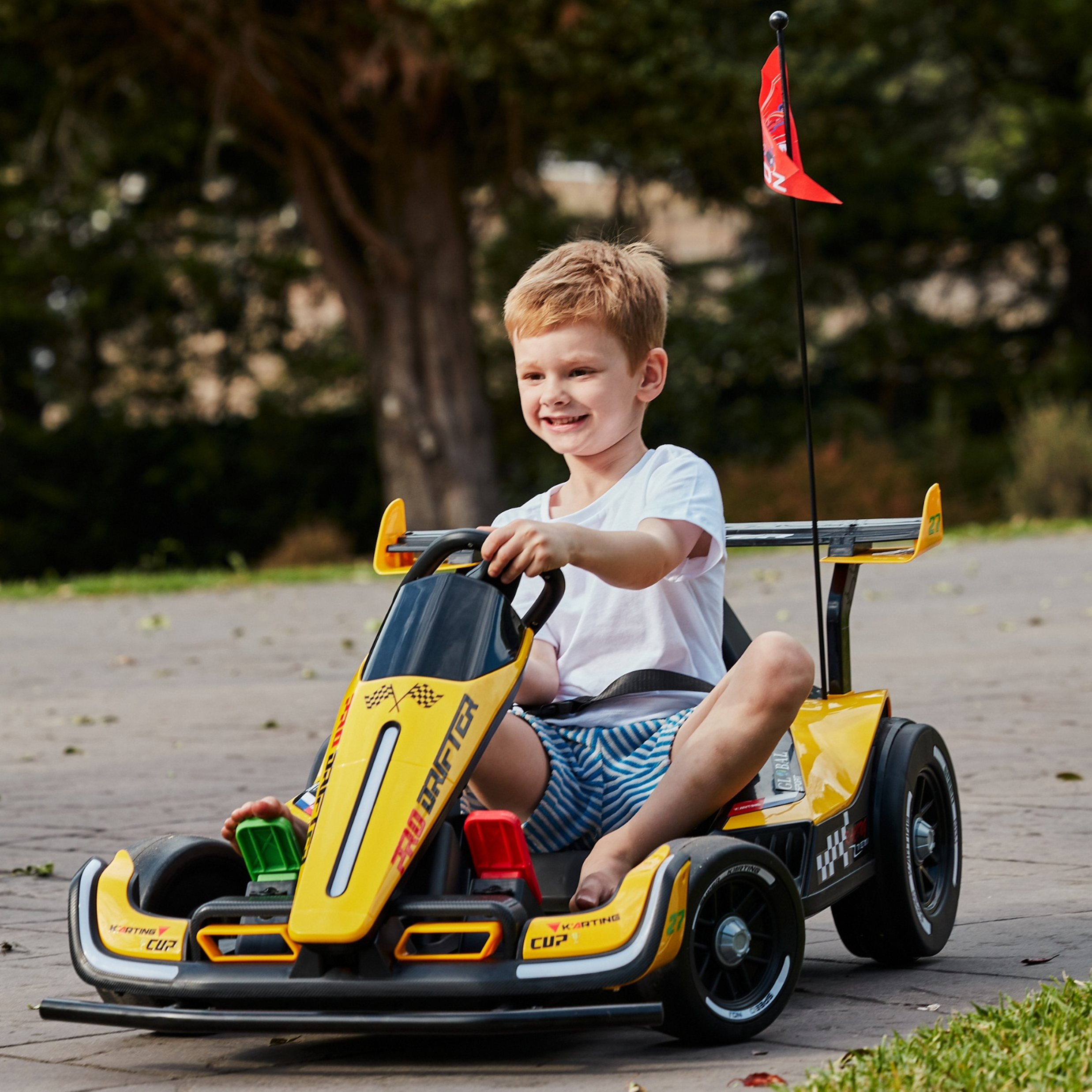 Child sitting in a toy car outdoors with trees in the background