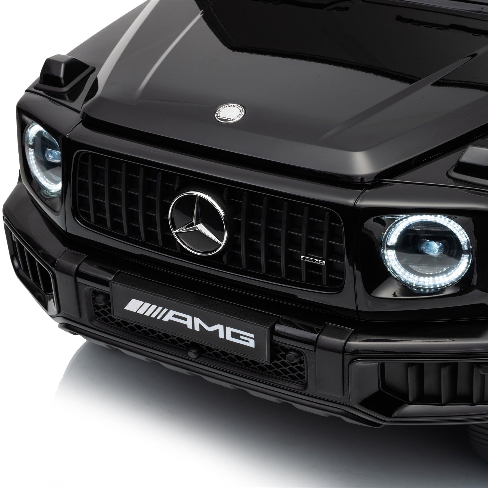 Close-up of a black Mercedes-Benz AMG vehicle front grille, headlights, hood, and front bumper on a clean white studio background.