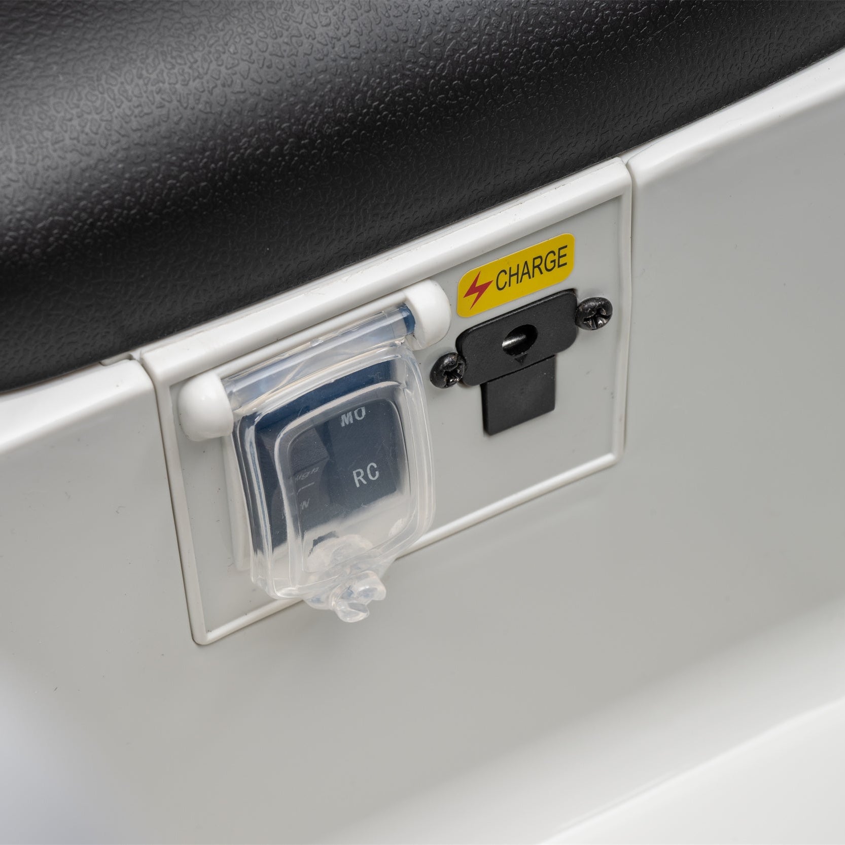 Close-up of a white vehicle or boat battery terminal cover with a black terminal and a yellow CHARGE sticker, next to a black textured surface.