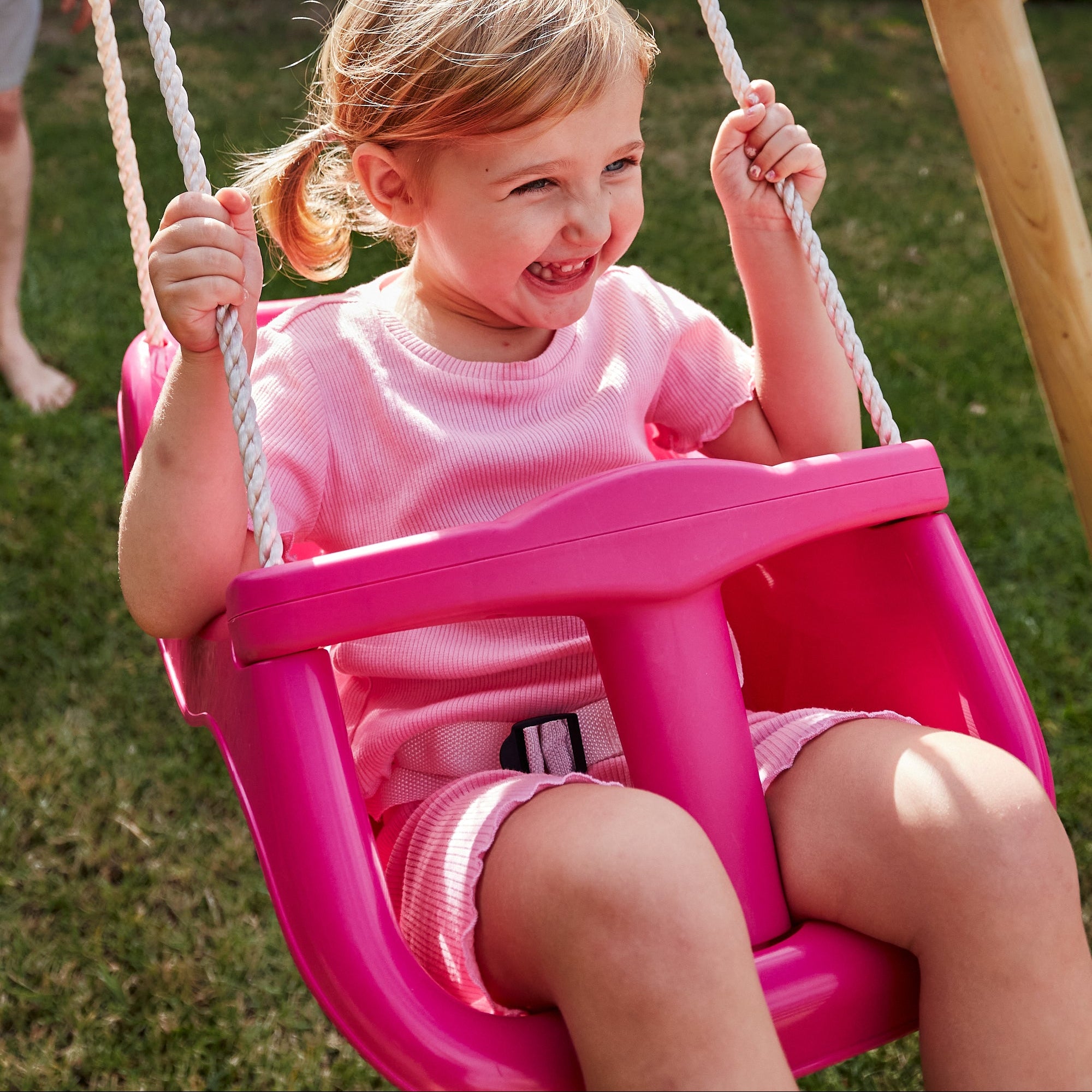 Child in a pink swing set on a grassy area