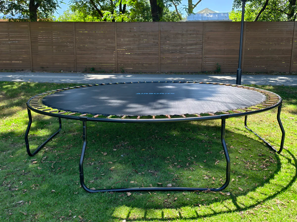 Trampoline in a backyard with a wooden fence and trees in the background