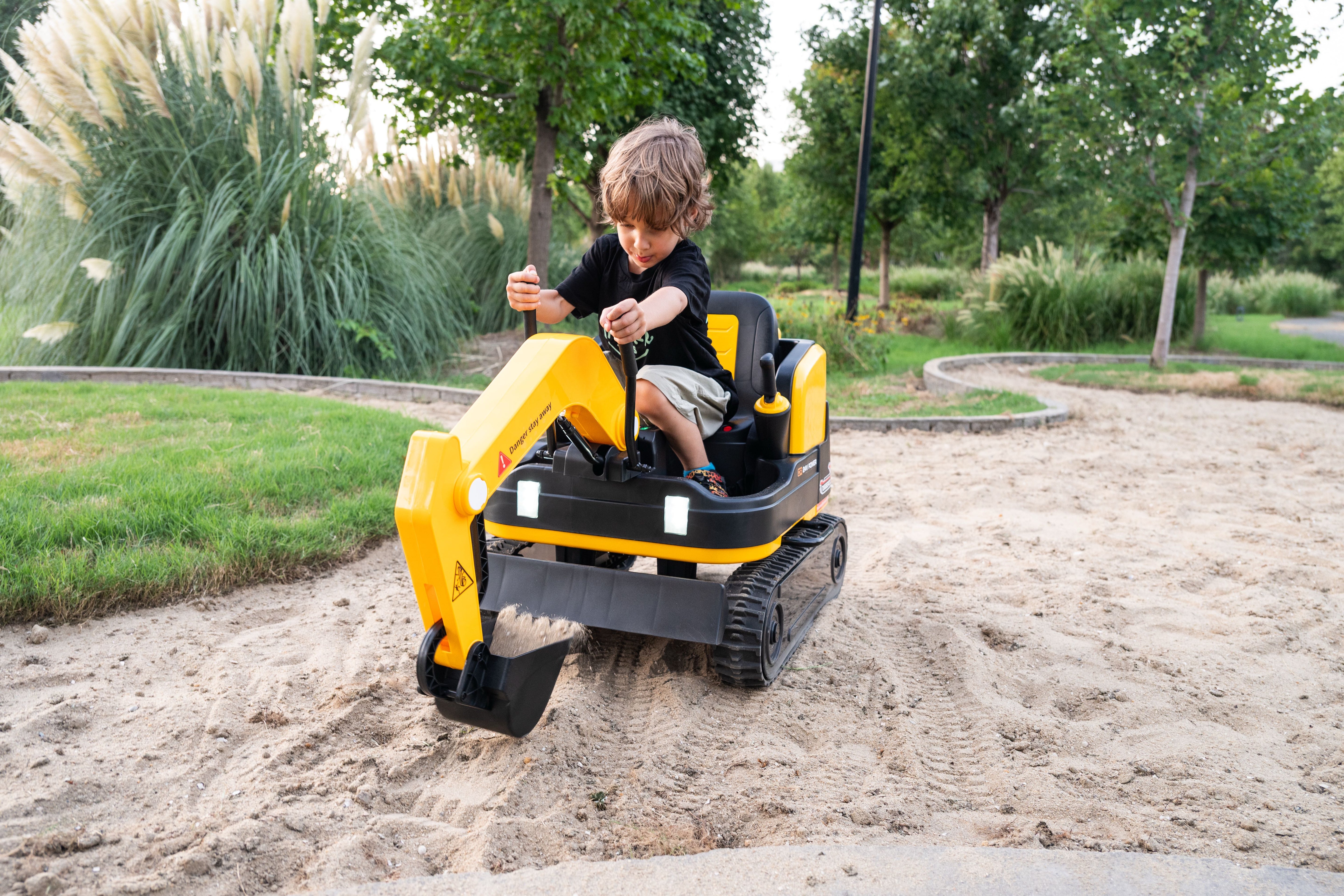 Child operating yellow 24V ride-on digger with parent supervising outdoors