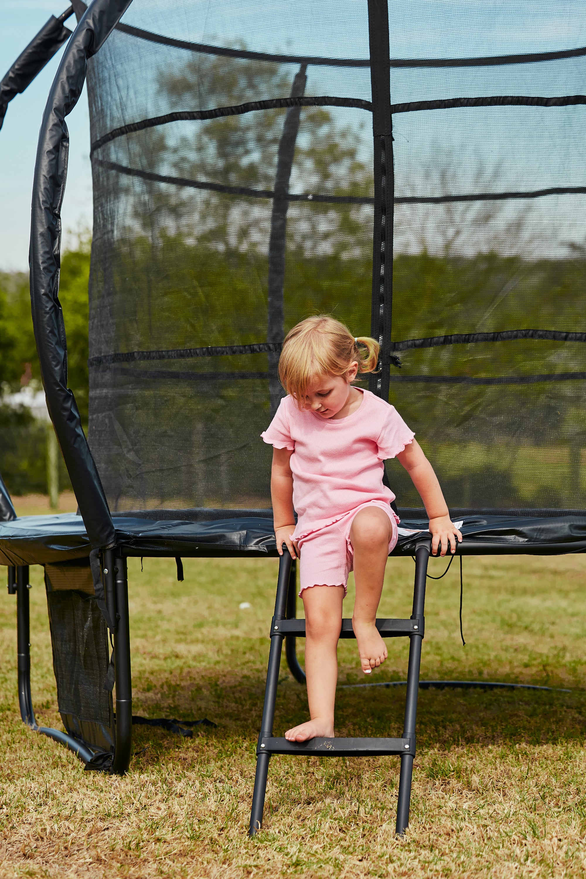 Child climbing down on a trampoline ladder in an outdoor setting