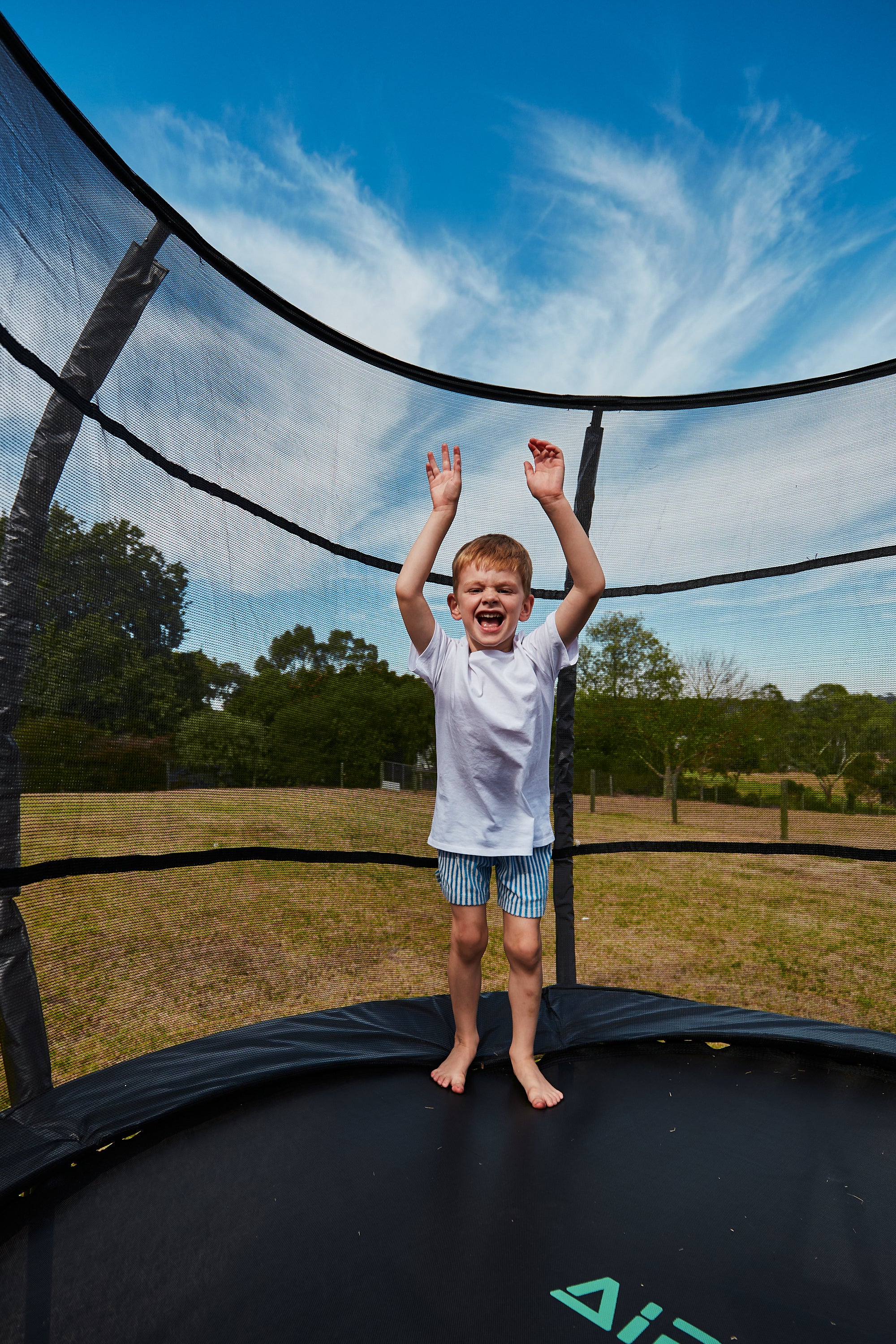 Child on a trampoline with a clear blue sky and trees in the background