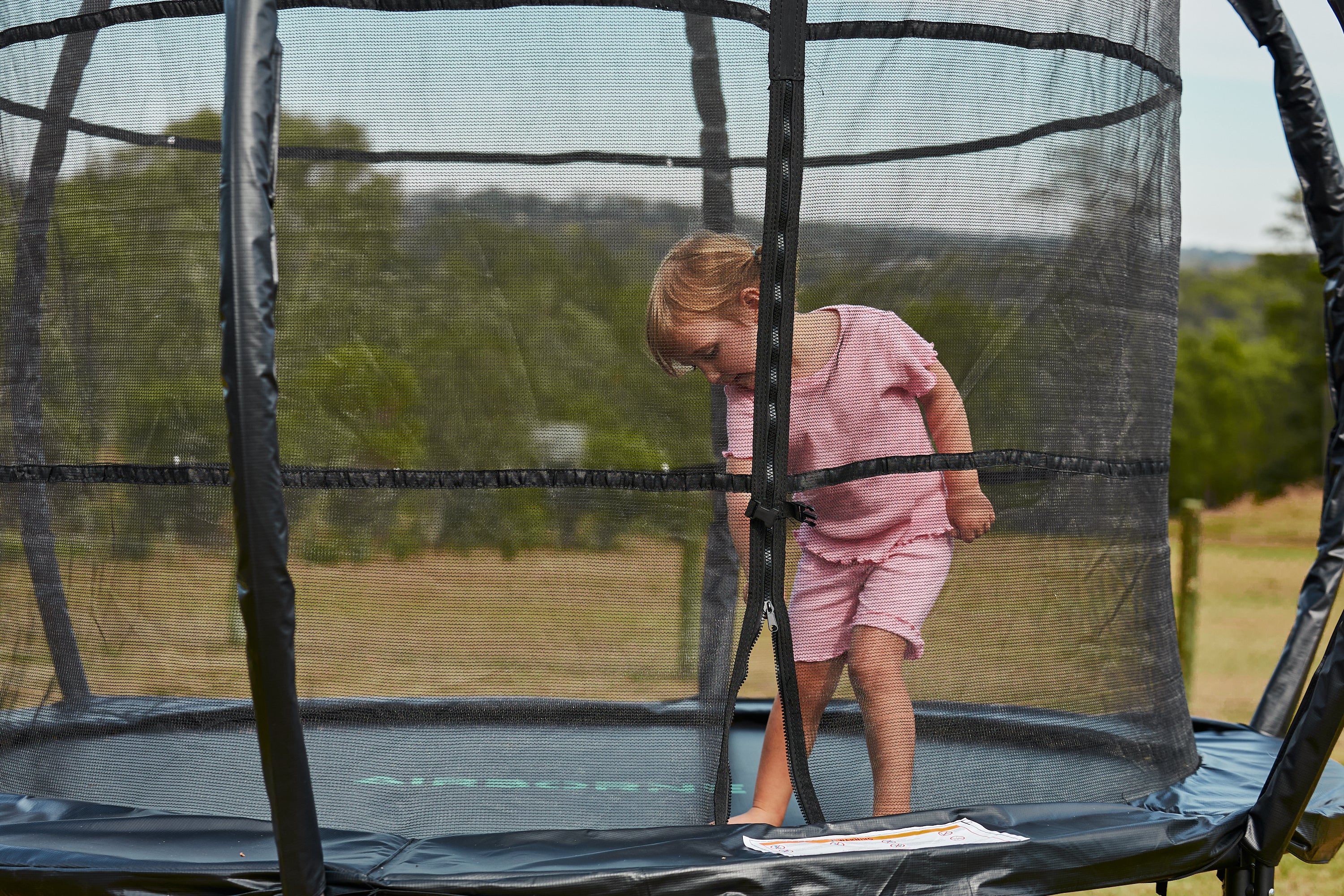 Child in pink outfit standing on a trampoline with a scenic background