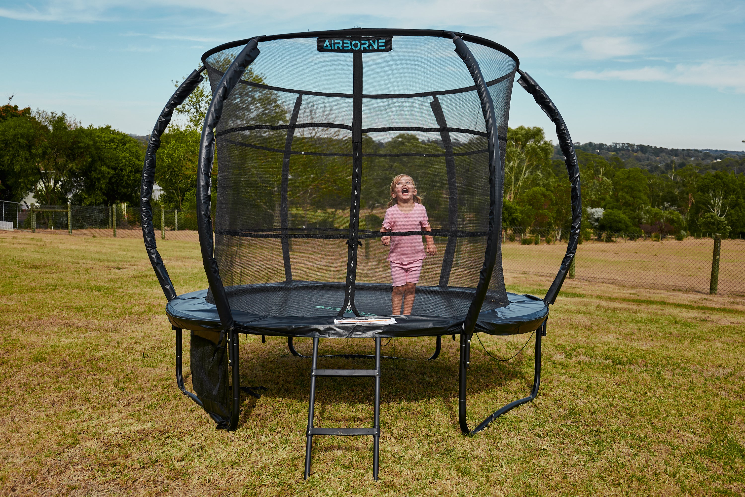 Child standing on a trampoline with safety net in an open field