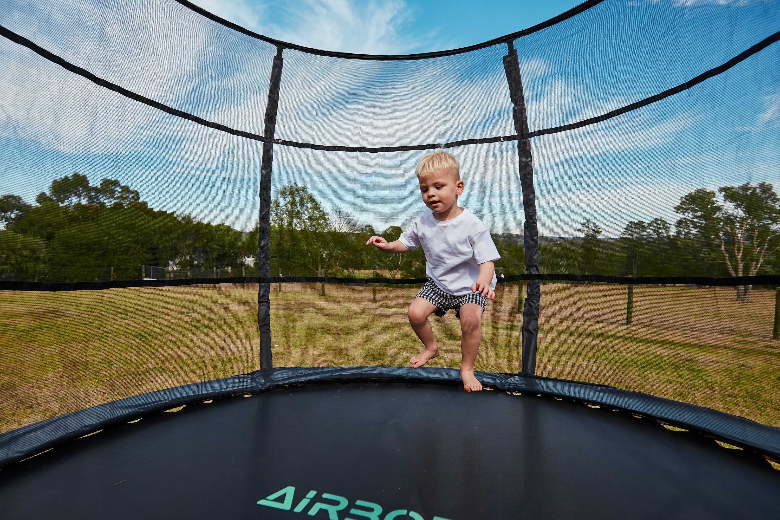 Child jumping on a trampoline with trees and sky in the background
