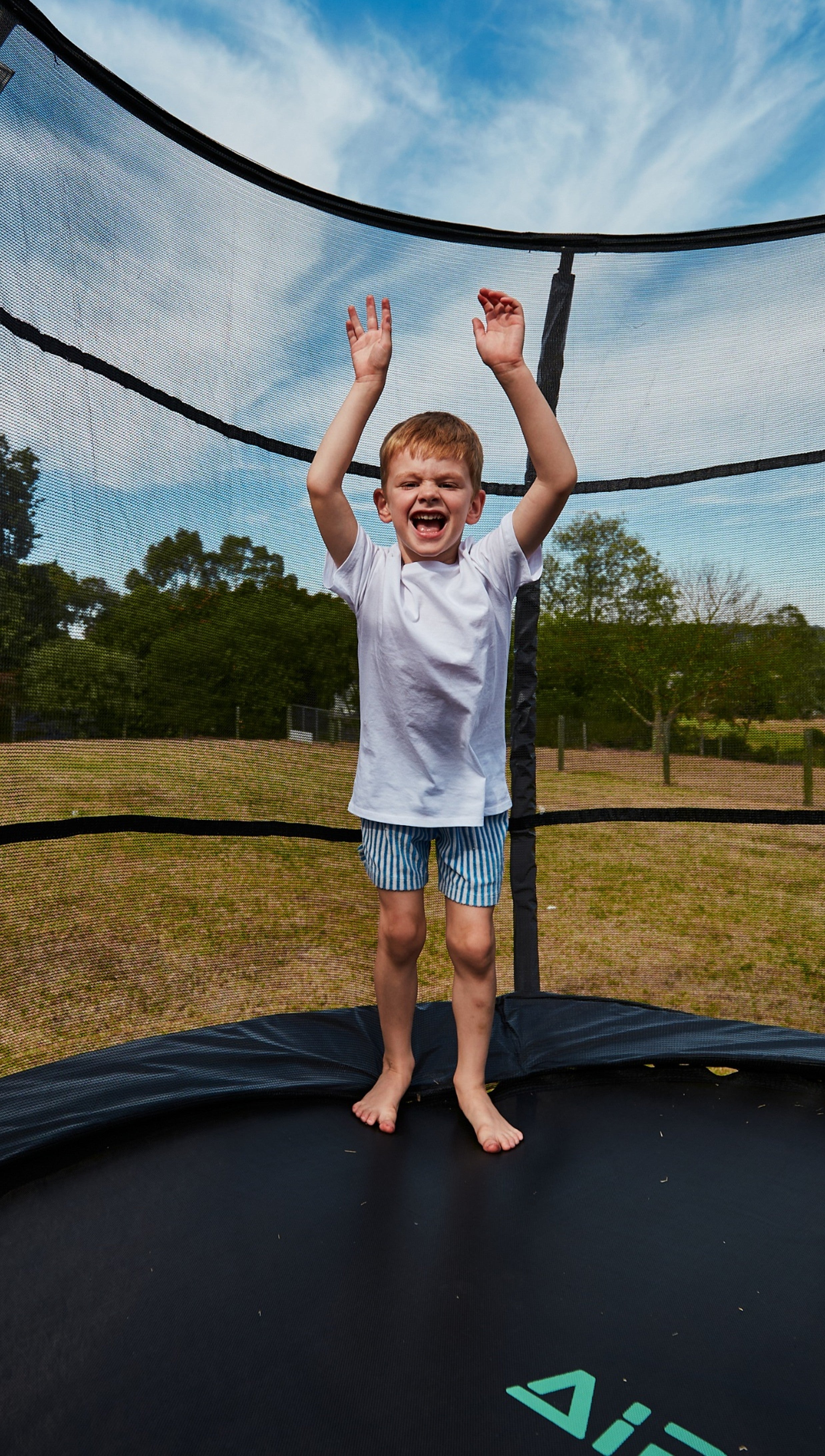 Child on a trampoline with a clear sky and trees in the background