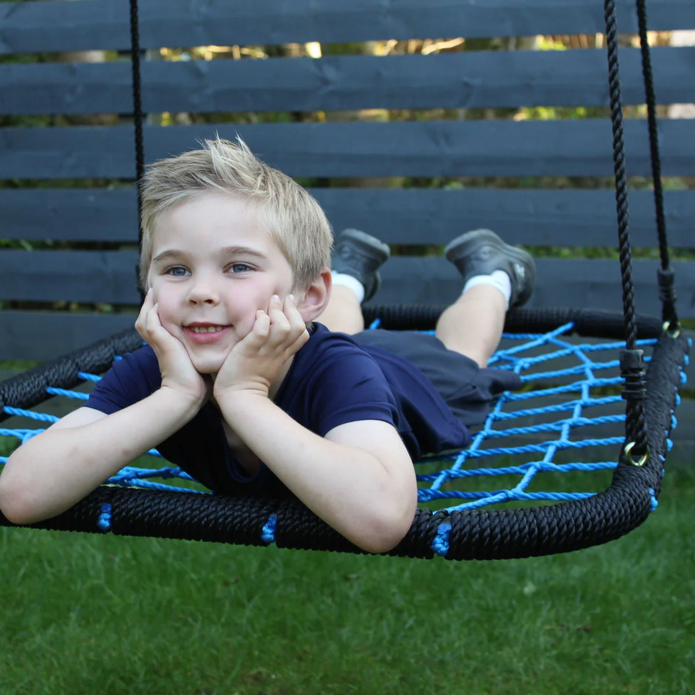 Child on a blue spider web swing in a garden