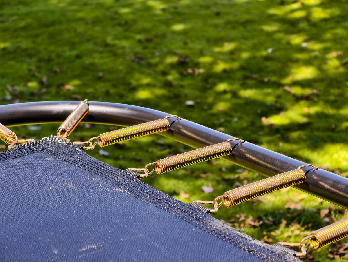Close-up of a trampoline spring with a grassy background