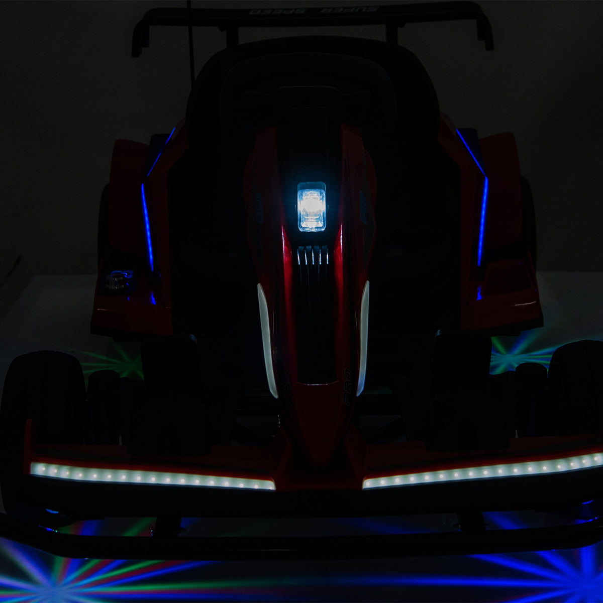 A red and black toy race car with illuminated LED lights, shown from the front on a dark background with blue and green light projections on the floor.