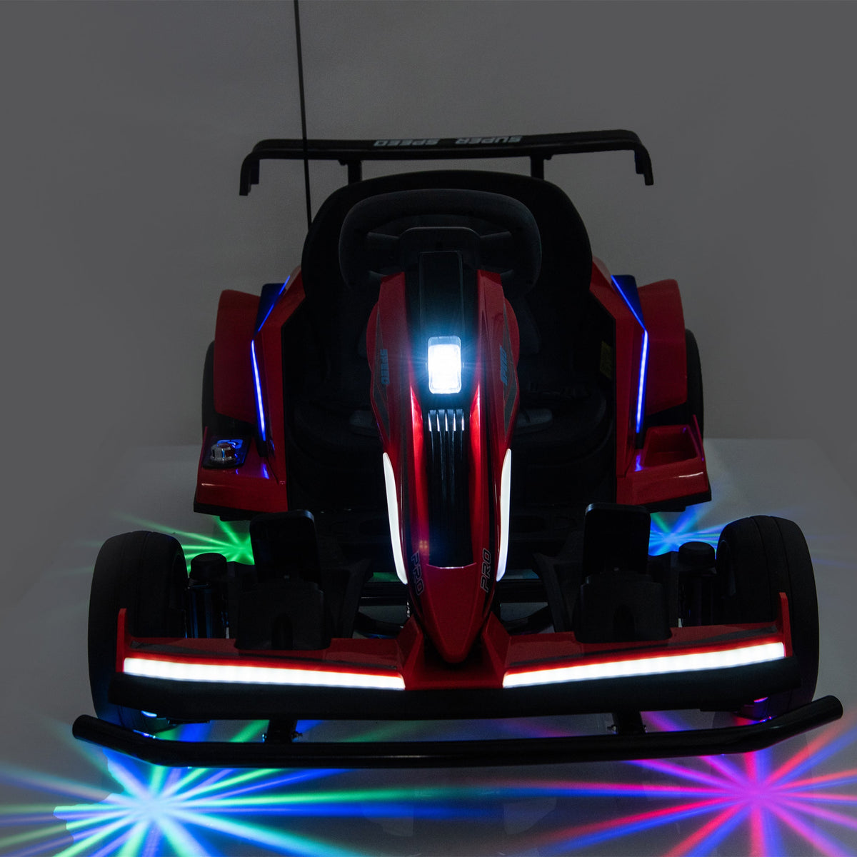 A red and black go-kart-style toy car shown from the front in a dark studio setting, with illuminated LED lights in blue, white, green, and pink reflecting on the floor.