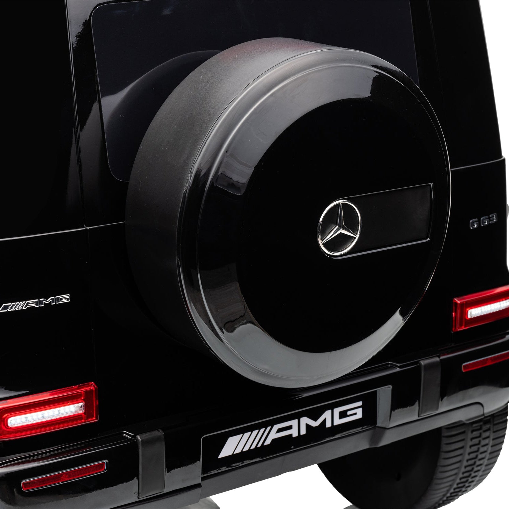 Close-up rear view of a black Mercedes-Benz G-Class vehicle showing the spare tire cover with the Mercedes star logo, AMG badge, and red taillights on a white background.
