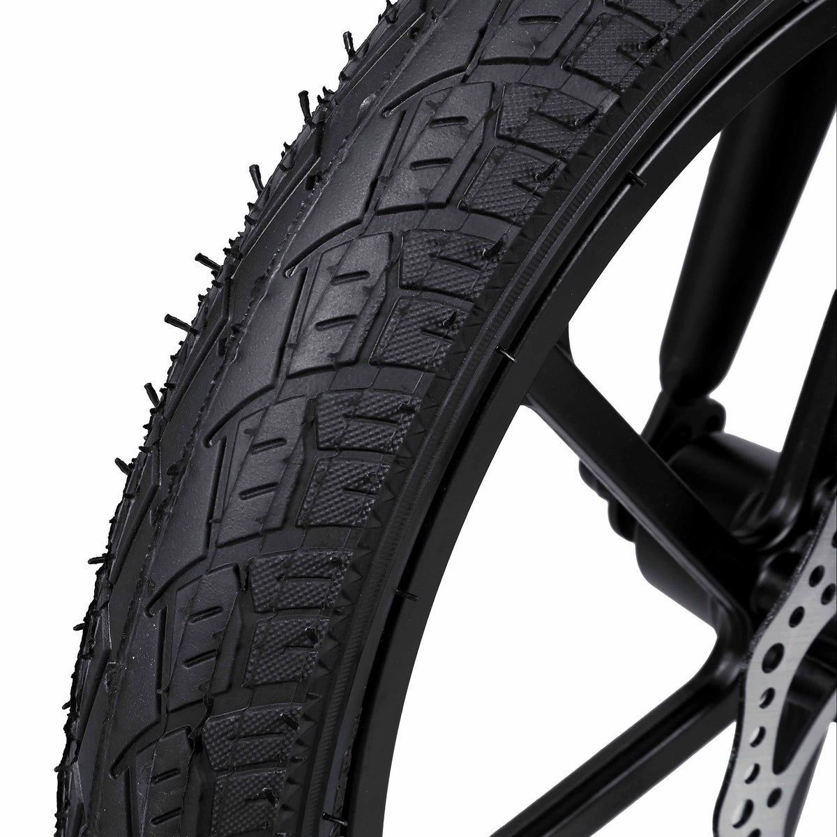 Close-up of a black off-road tire with aggressive tread, mounted on a black wheel with a visible disc brake, set against a solid white background.