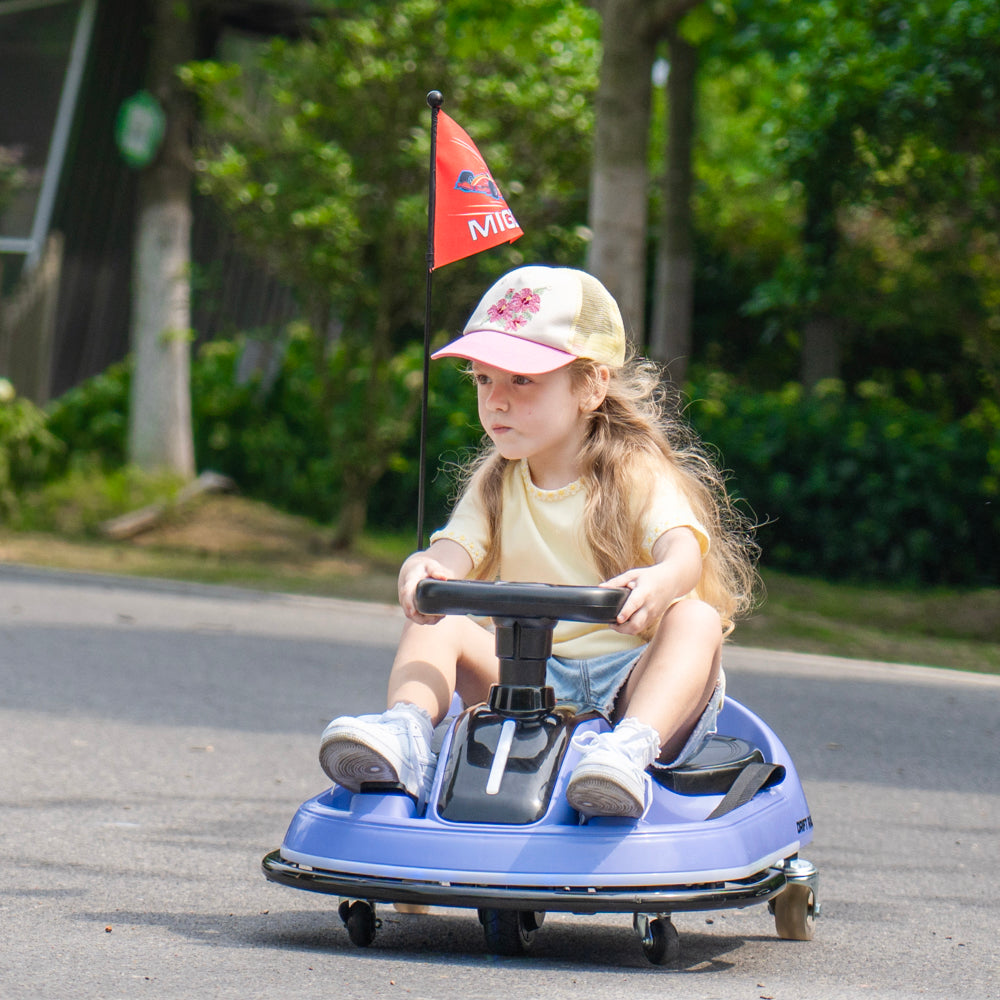 A young girl wearing a beige cap and a yellow t-shirt sits on a blue pedal toy car on an outdoor paved road, with green trees in the background.