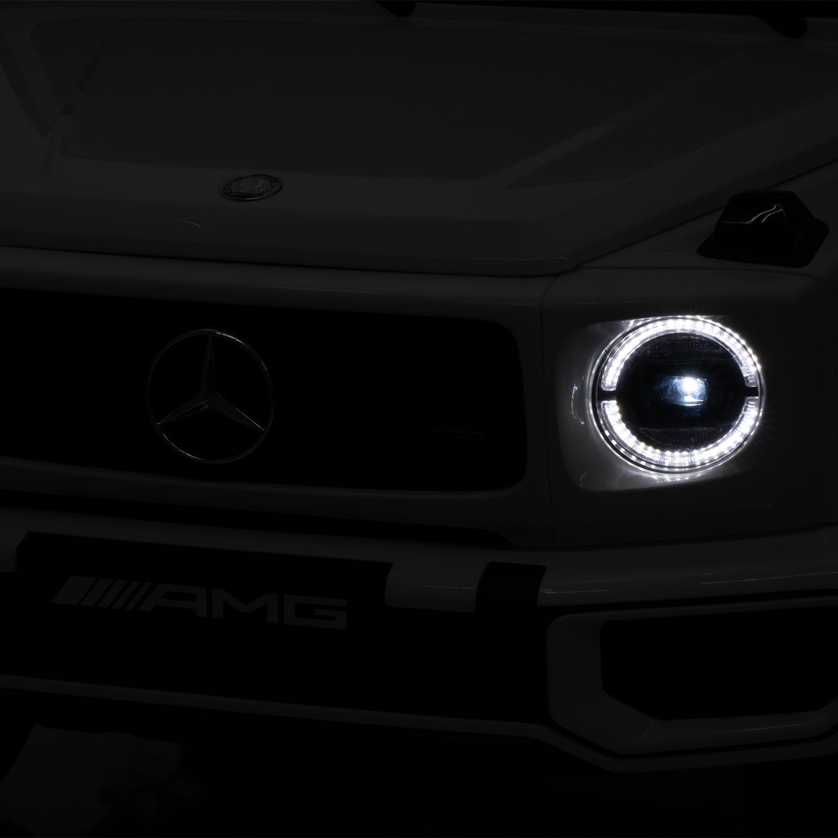 Close-up of a Mercedes-AMG vehicle front grille and headlights in very low light, showing the Mercedes star emblem and AMG badge.
