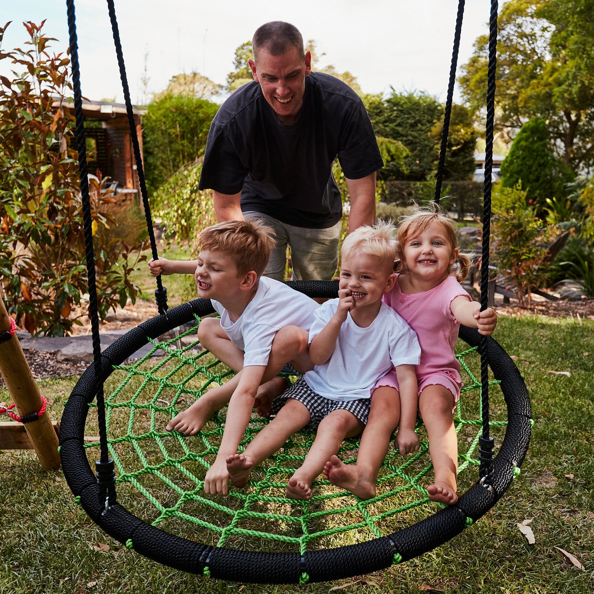 Man and three children on a spider web swing in a backyard setting