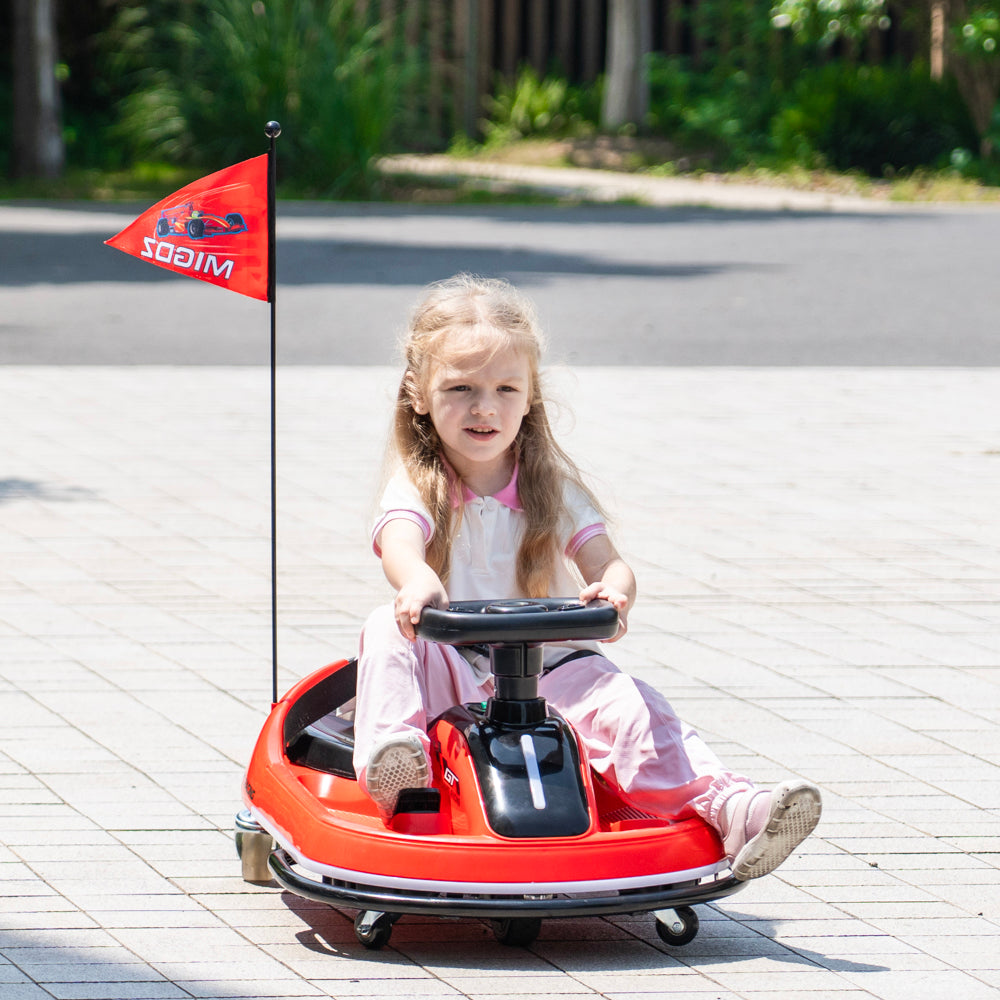 A young girl with blonde hair sits in a red go-kart on a paved outdoor surface. The go-kart has a small red flag on a pole behind her with the word 'WILD' visible.