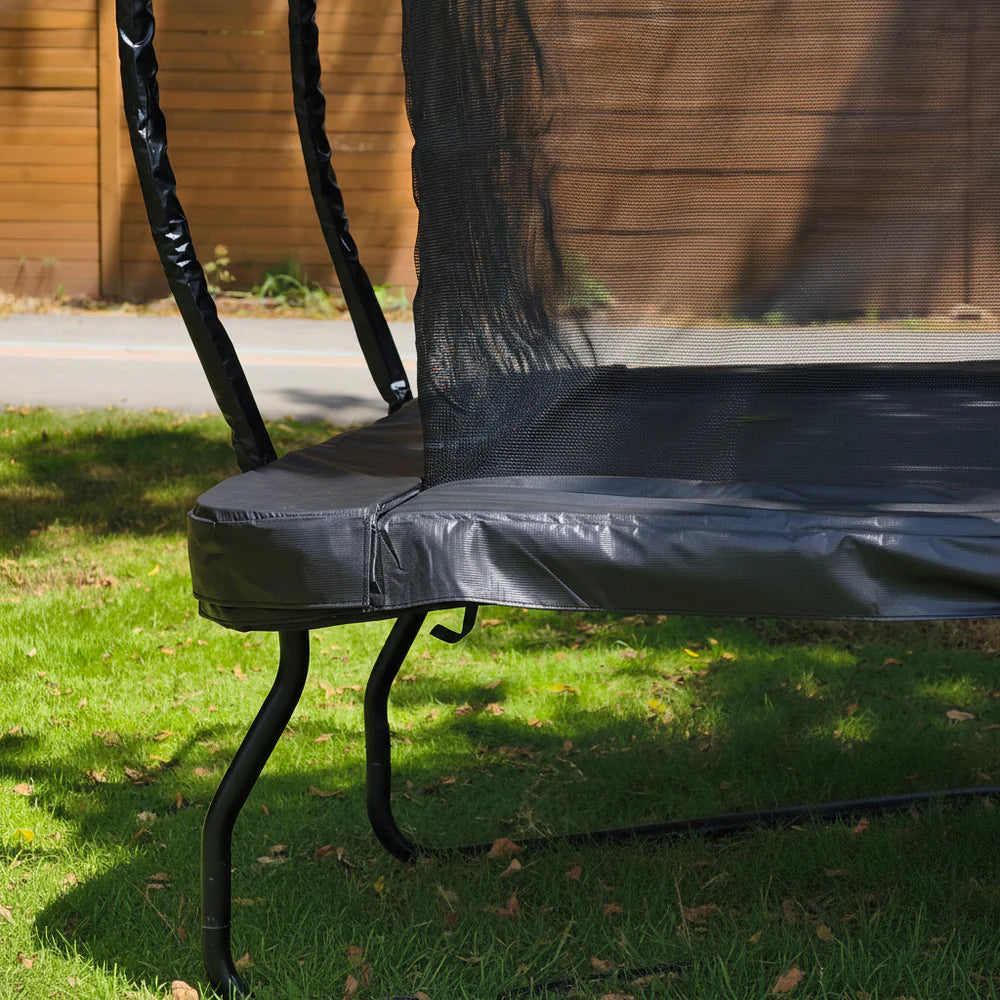 Black trampoline on grass with wooden fence in the background