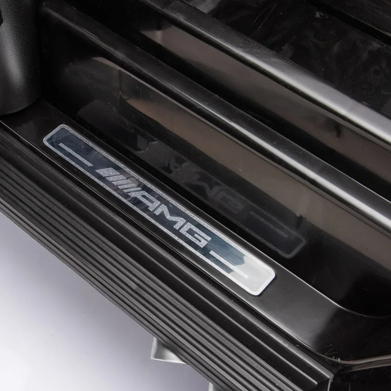 Close-up of a black car door sill featuring a silver AMG logo badge on a white vehicle interior.