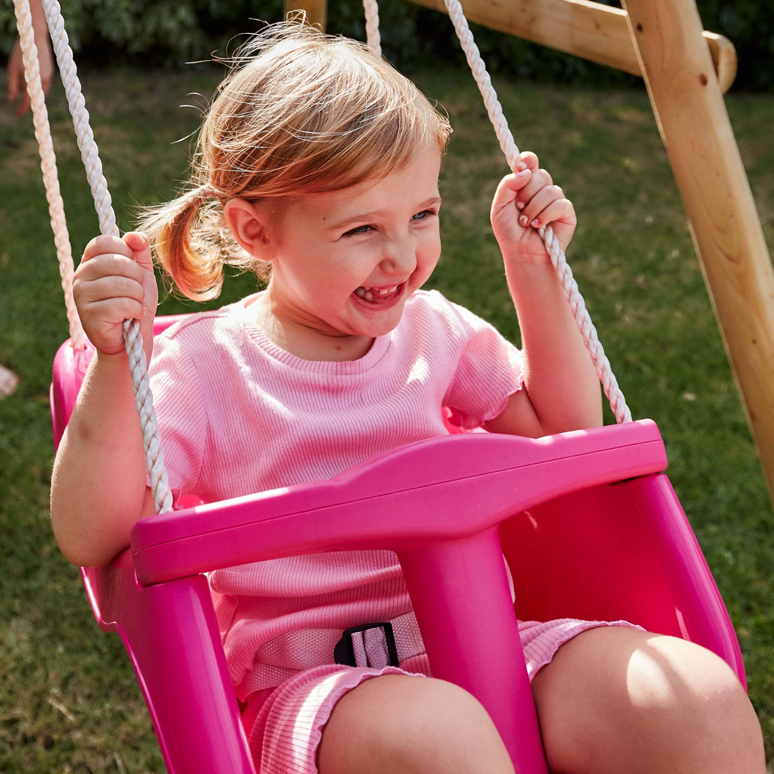 Child in a pink swing set on a grassy area