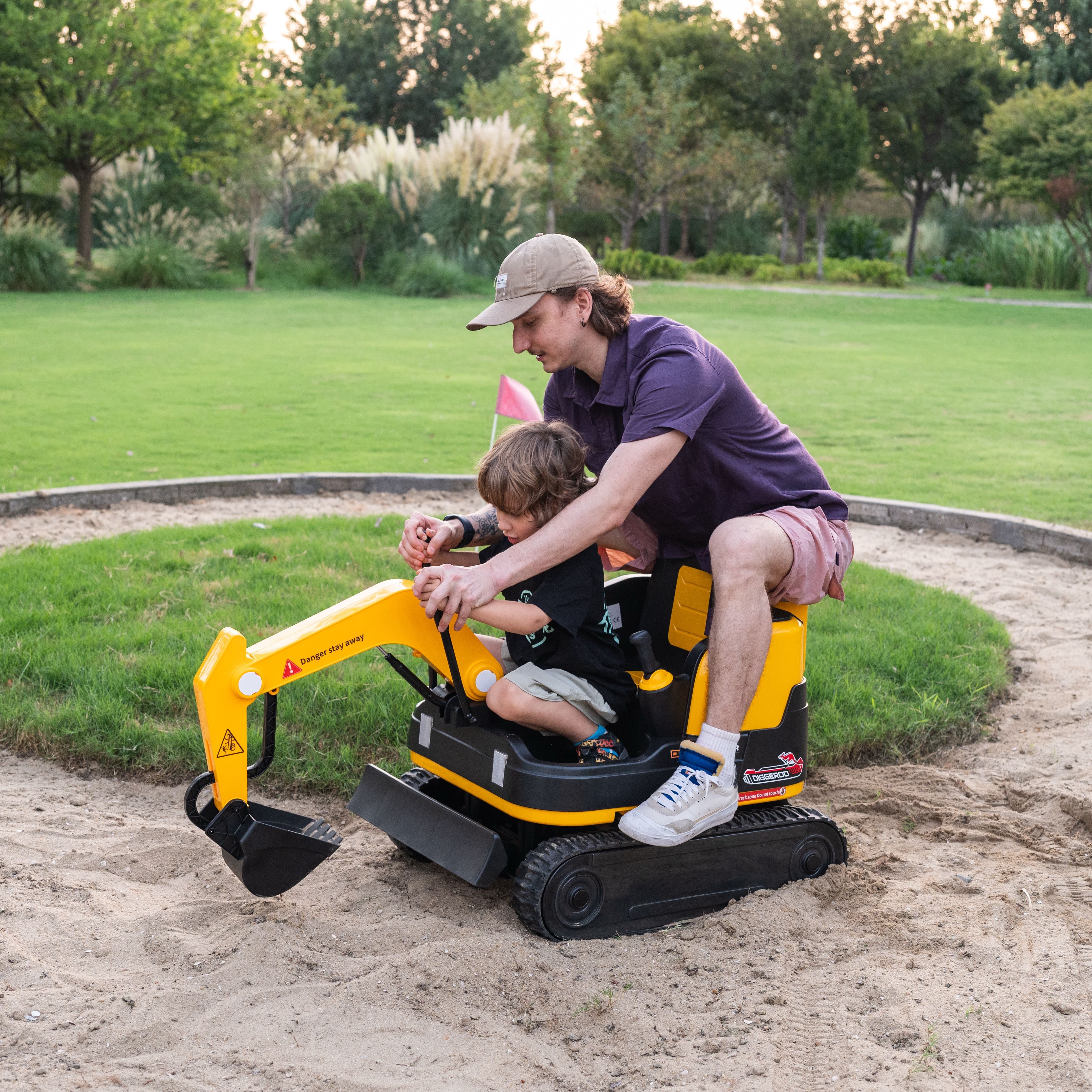 Child playing with a toy excavator in a park with an adult supervising