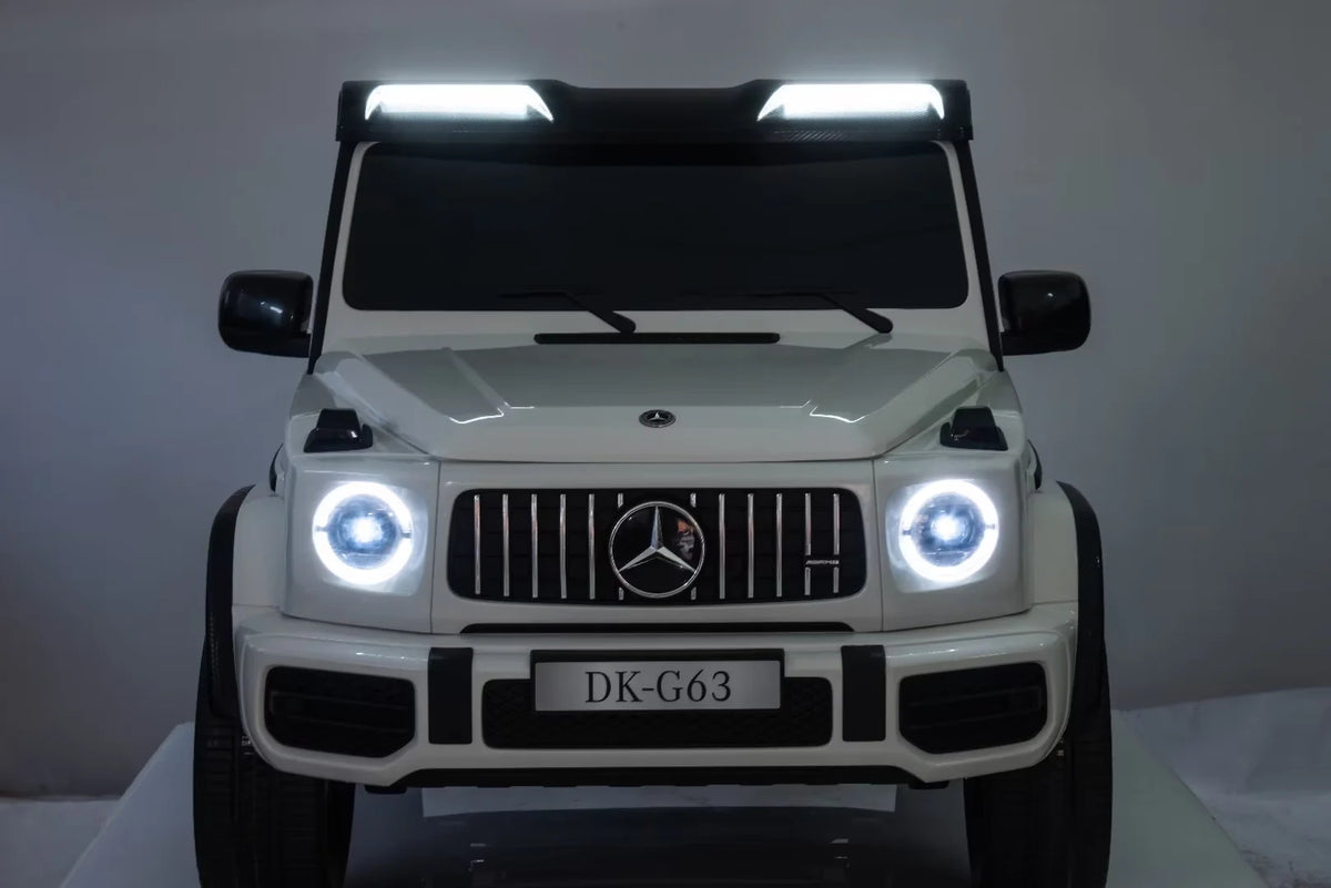 A white Mercedes-Benz G-Class style children's ride-on toy truck photographed from the front, with the Mercedes star grille and illuminated headlights visible, on a plain studio background.