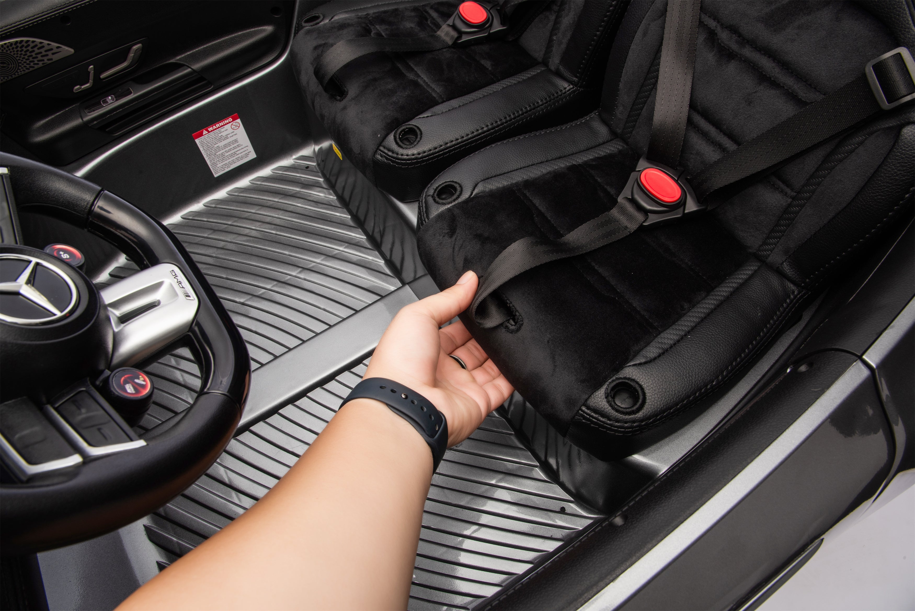 Person adjusting a black car seat in a vehicle with a Mercedes-Benz steering wheel.