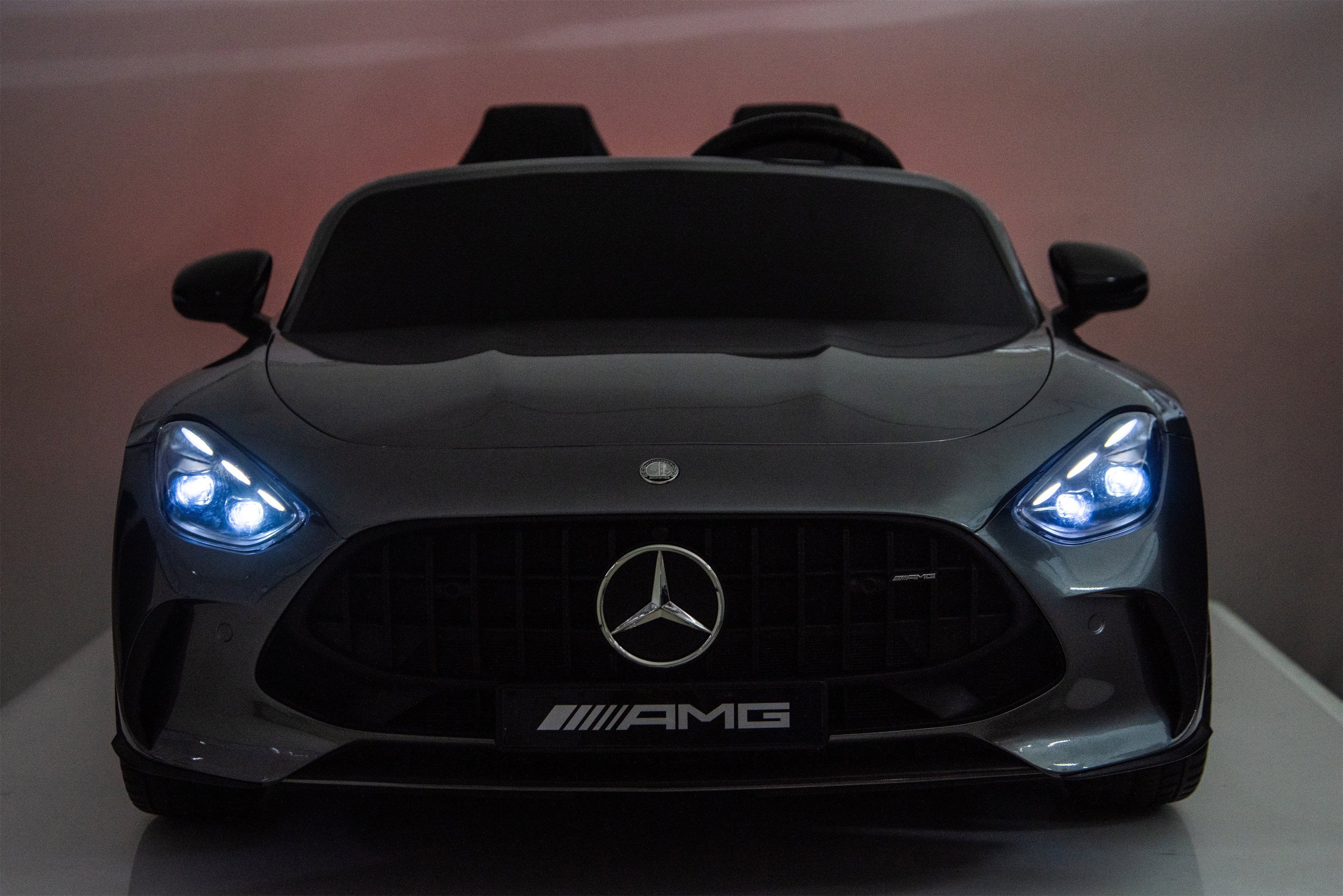 Front view of a Mercedes-Benz AMG toy car with glowing headlights on a reflective surface.