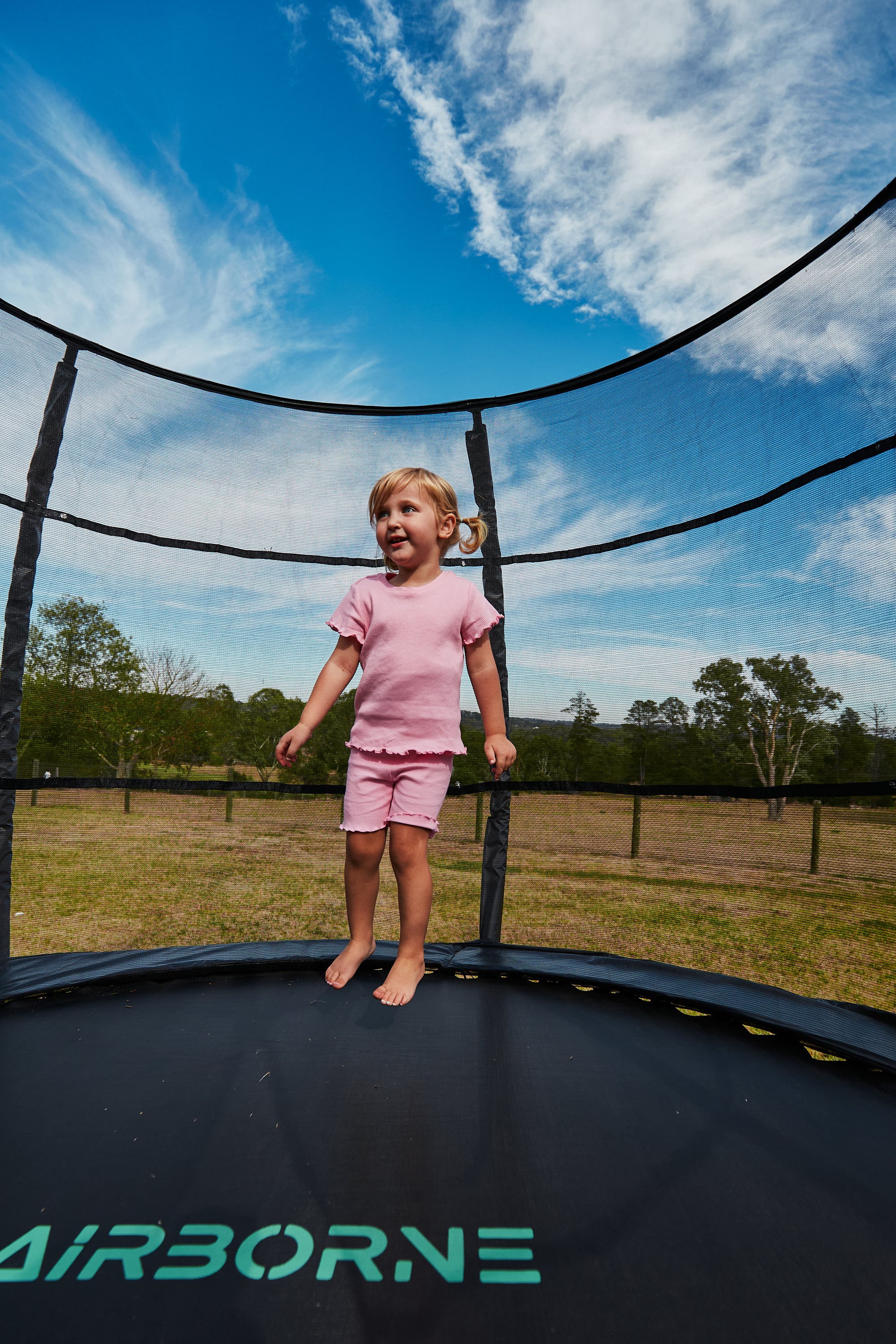 Child on a trampoline with a clear blue sky and trees in the background