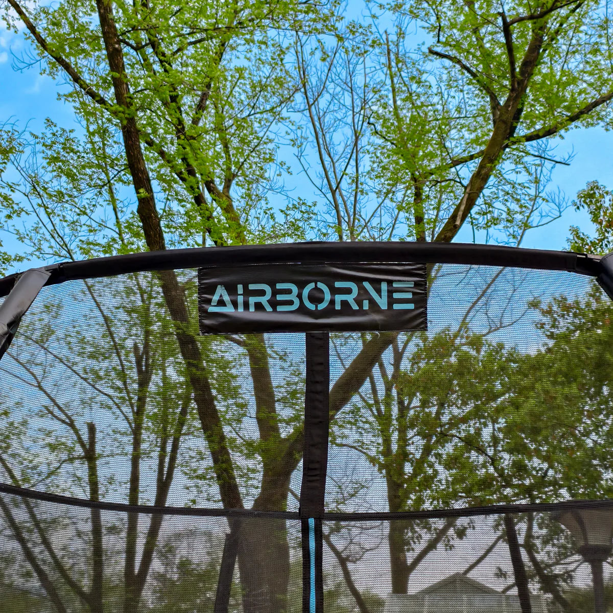 Trampoline with 'AIRBORNE' branding against a backdrop of trees and blue sky.