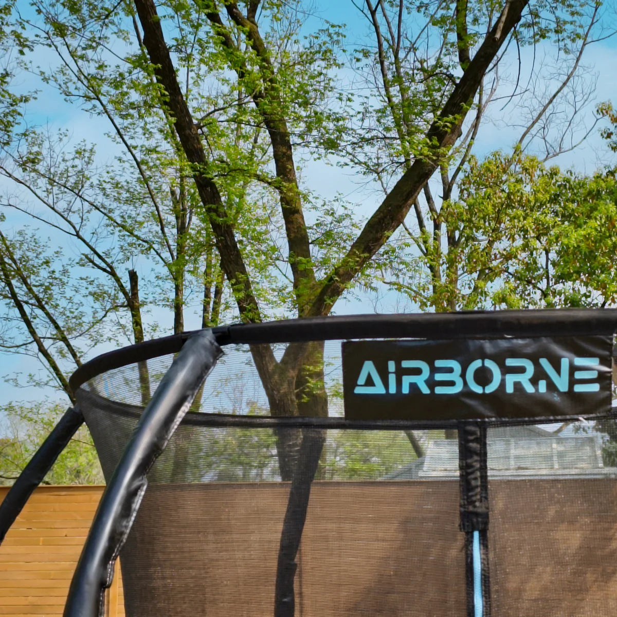 Trampoline with 'AiRBORNE' branding against a backdrop of trees and clear sky