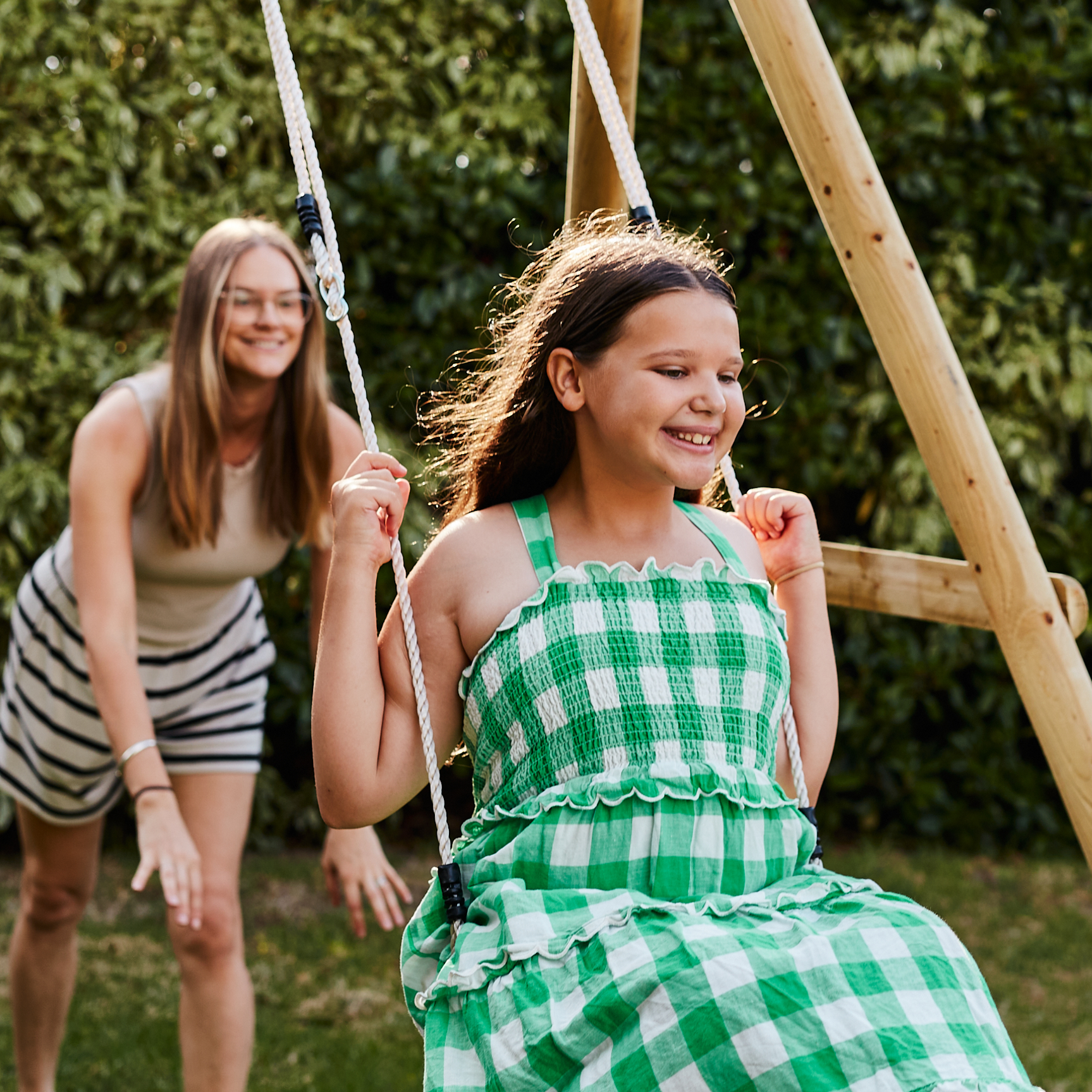 Two girls playing on a swing set in a garden.